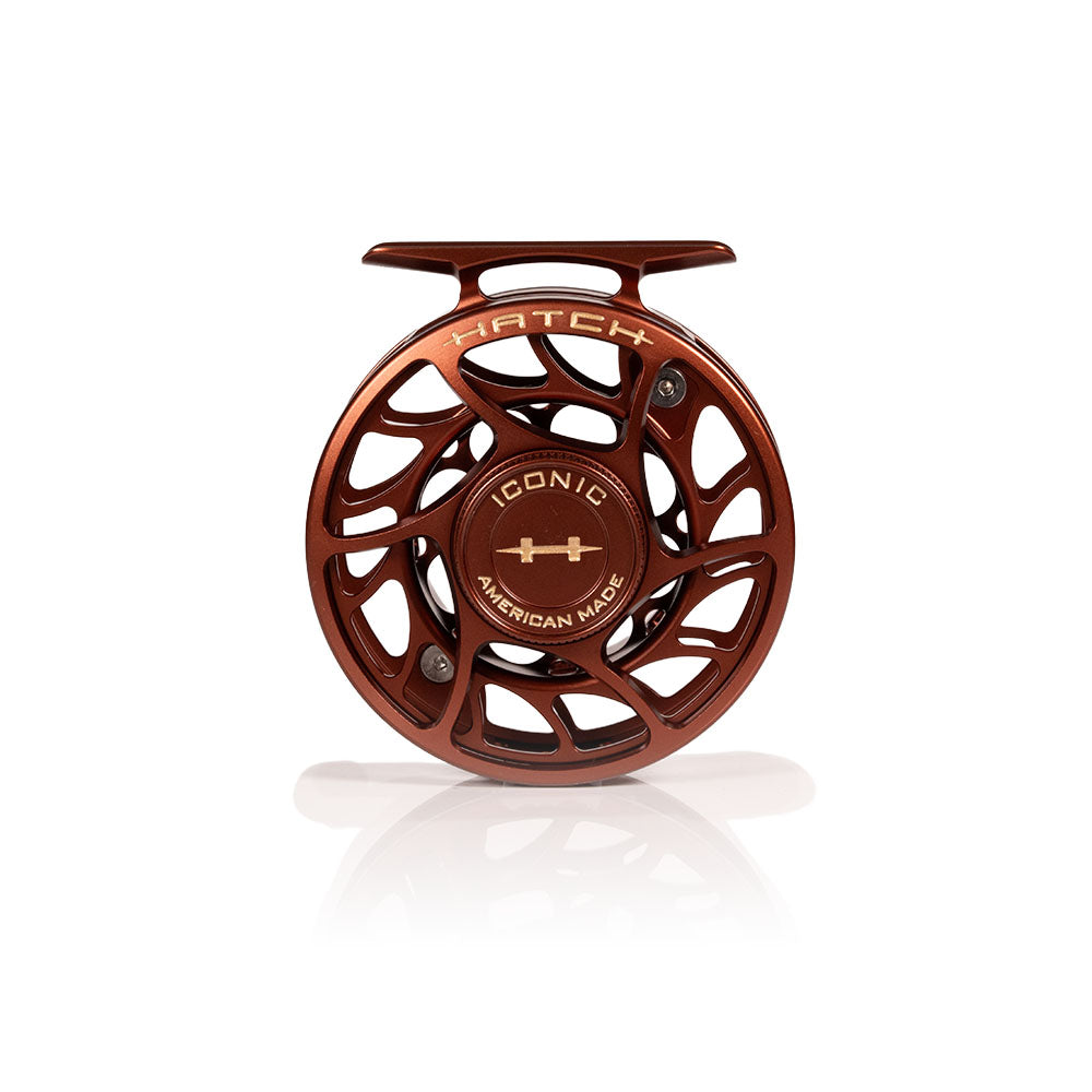 A copper-colored aluminum fly fishing reel on a clean white background with a soft reflection underneath. The reel features the brand name 'HATCH' and model name 'ICONIC AMERICAN HATCH' printed on its face.